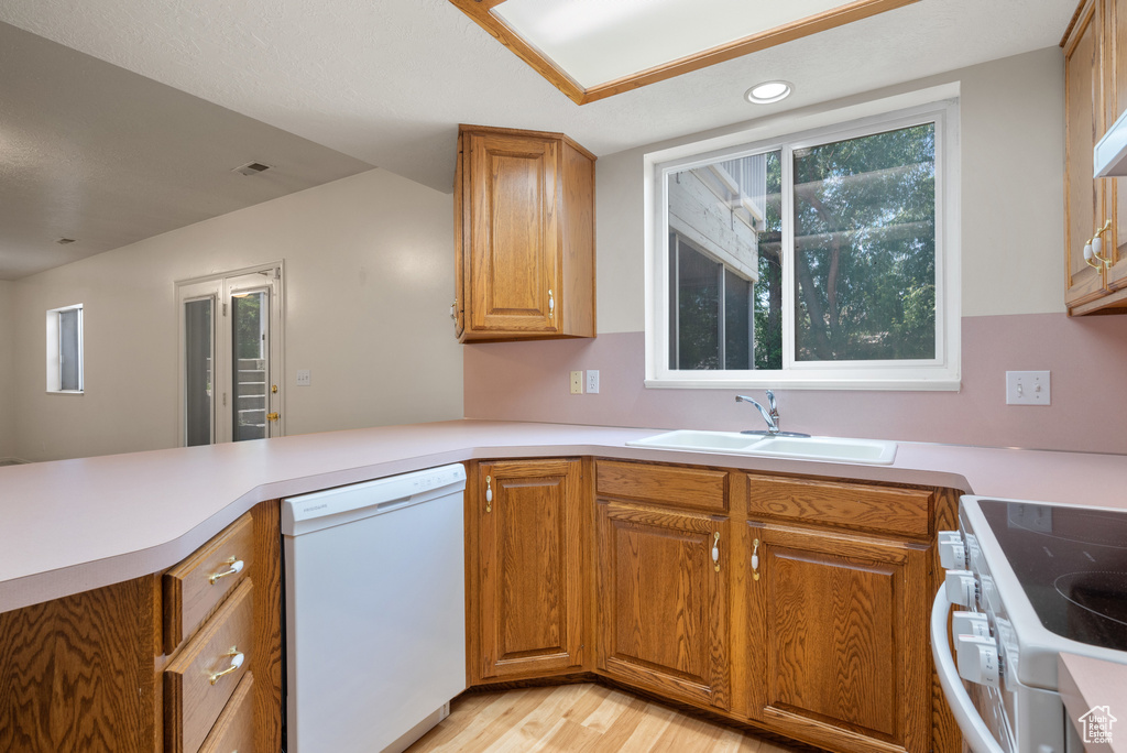Kitchen featuring white appliances, light wood-type flooring, a peninsula, brown cabinetry, and light countertops