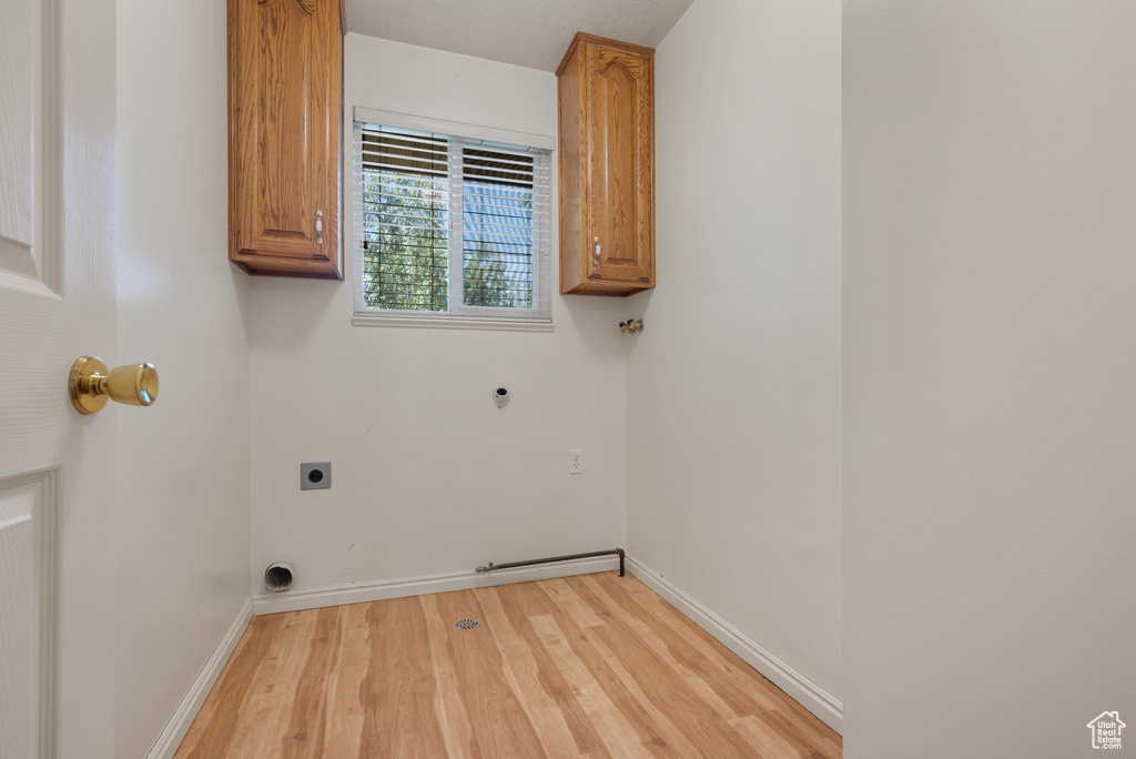 Washroom featuring electric dryer hookup, cabinet space, light wood-type flooring, and hookup for a gas dryer
