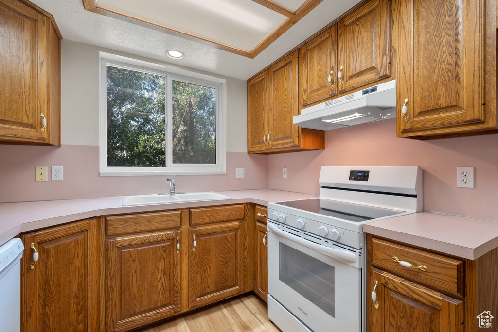 Kitchen featuring white appliances, under cabinet range hood, and brown cabinets