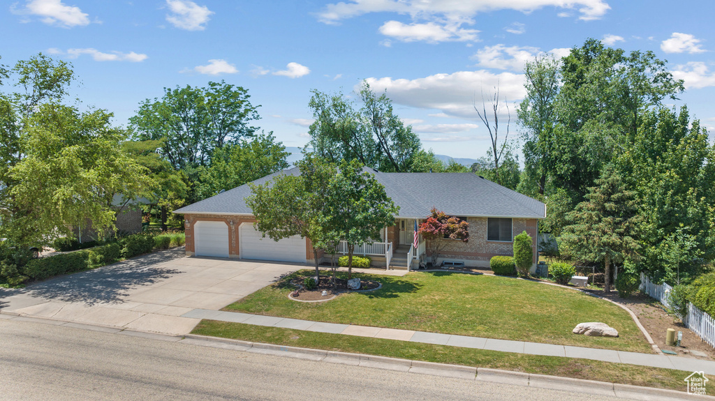 View of front of house with driveway, a front yard, a garage, roof with shingles, and brick siding
