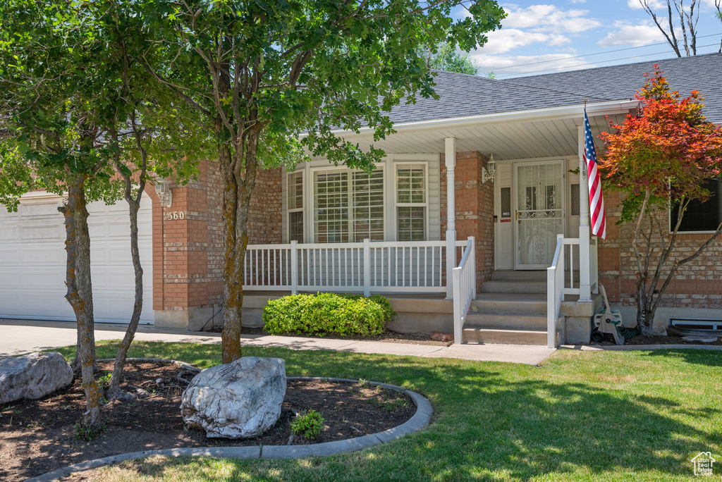 View of front of home featuring covered porch, brick siding, a shingled roof, and a front lawn