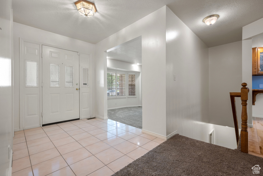 Foyer entrance with light carpet, light tile patterned floors, and a textured ceiling