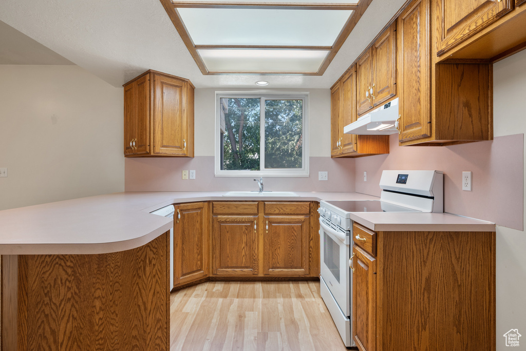 Kitchen with white electric range oven, under cabinet range hood, brown cabinets, and a peninsula