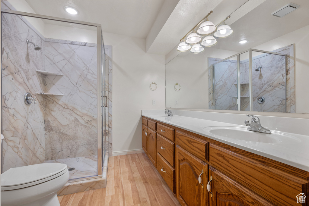 Full bath featuring double vanity, a marble finish shower, and wood finished floors