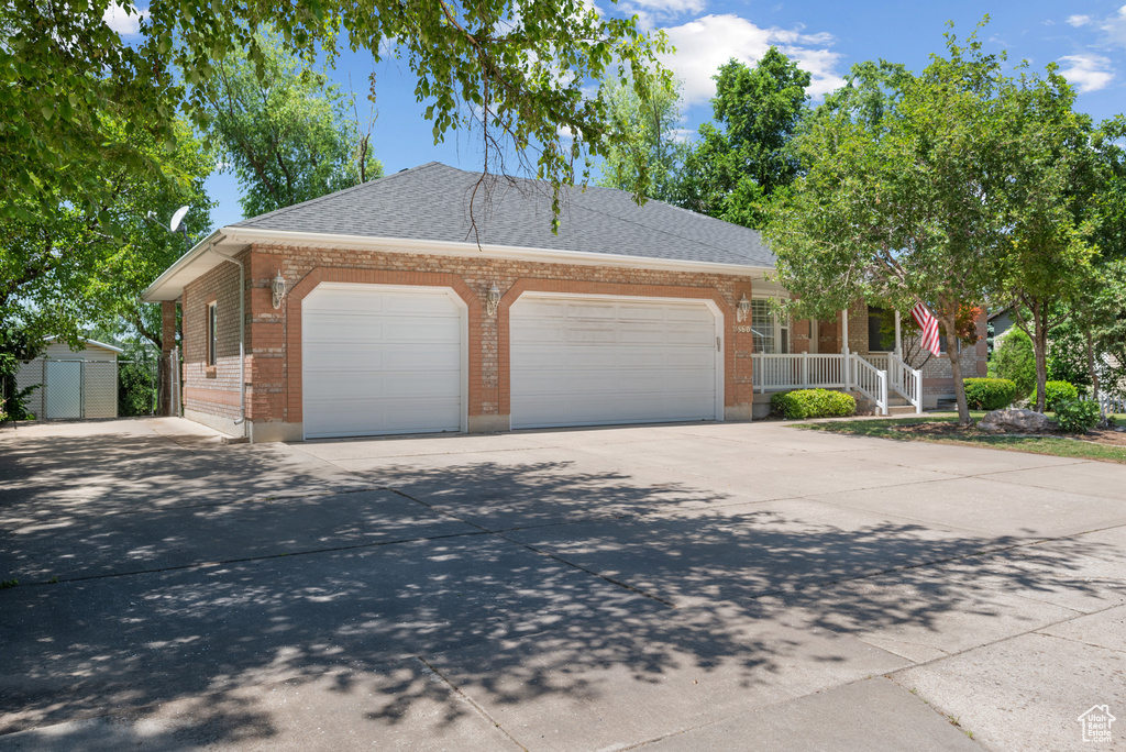 View of front of home featuring a garage, brick siding, driveway, a porch, and a storage shed