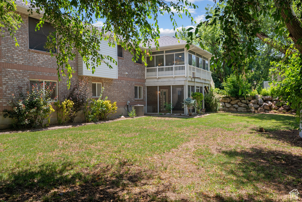 Back of property featuring a sunroom, brick siding, and a yard