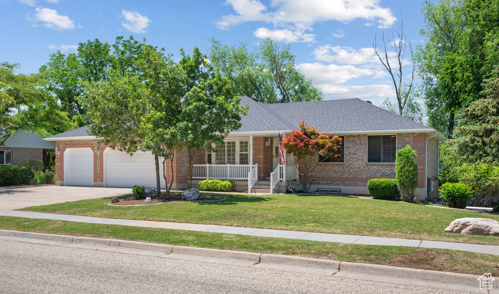 View of front of house with brick siding, a porch, a garage, concrete driveway, and a front yard