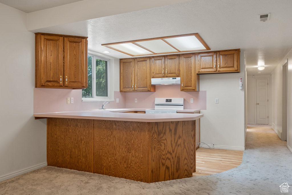 Kitchen featuring under cabinet range hood, white electric range, a peninsula, and brown cabinets