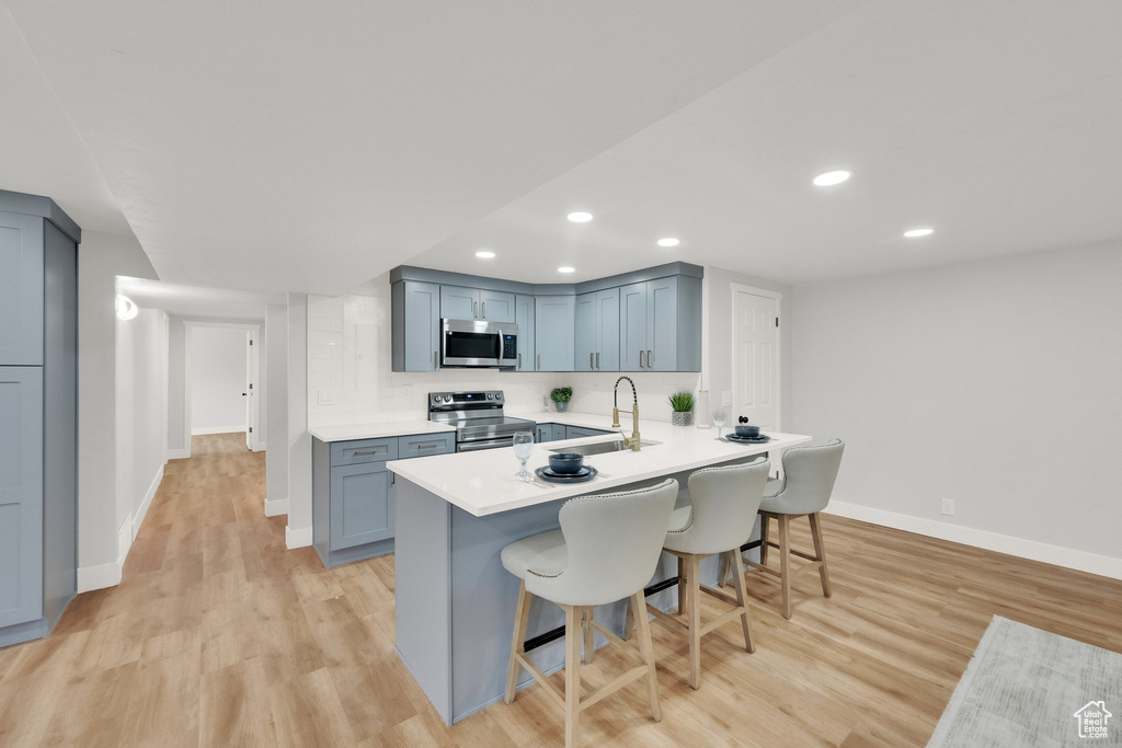 Kitchen with stainless steel appliances, a breakfast bar, light wood-style flooring, a peninsula, and recessed lighting