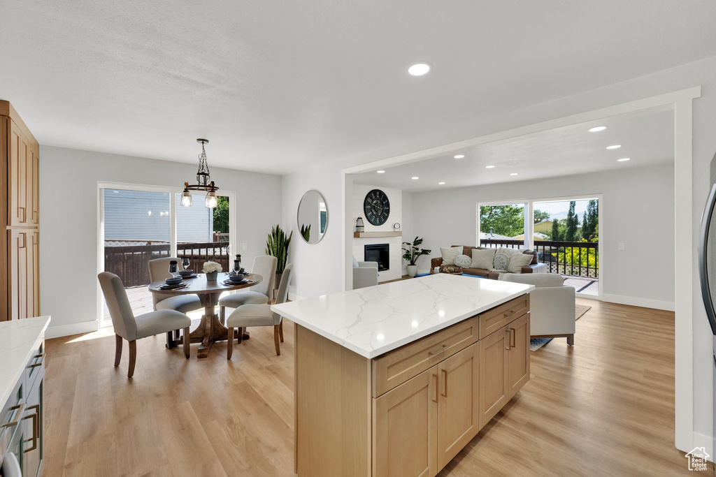 Kitchen with light wood-type flooring, open floor plan, a center island, recessed lighting, and a glass covered fireplace