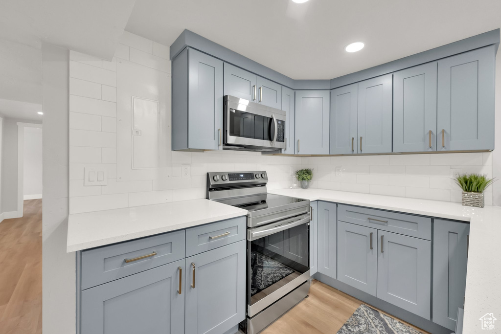 Kitchen with appliances with stainless steel finishes, light wood finished floors, backsplash, gray cabinets, and light countertops