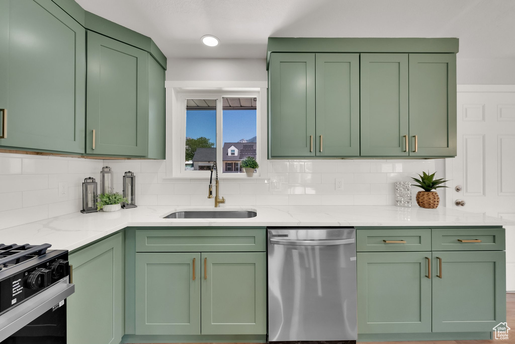 Kitchen with dishwasher, green cabinets, light stone counters, decorative backsplash, and range with gas stovetop
