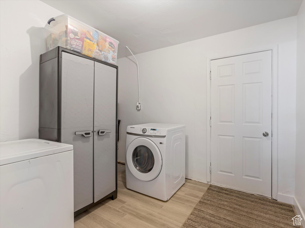 Laundry area featuring washing machine and dryer, cabinet space, and light wood-type flooring