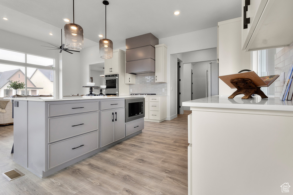 Kitchen featuring built in microwave, custom exhaust hood, gray cabinets, decorative backsplash, and light wood-style floors