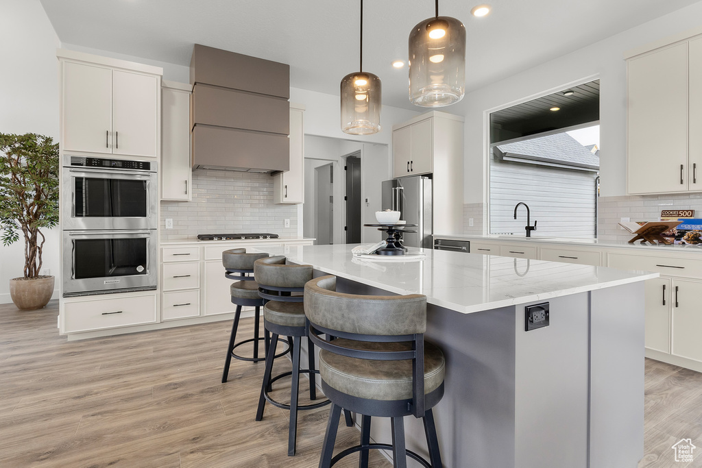 Kitchen with stainless steel appliances, backsplash, a kitchen breakfast bar, light wood-type flooring, and a kitchen island