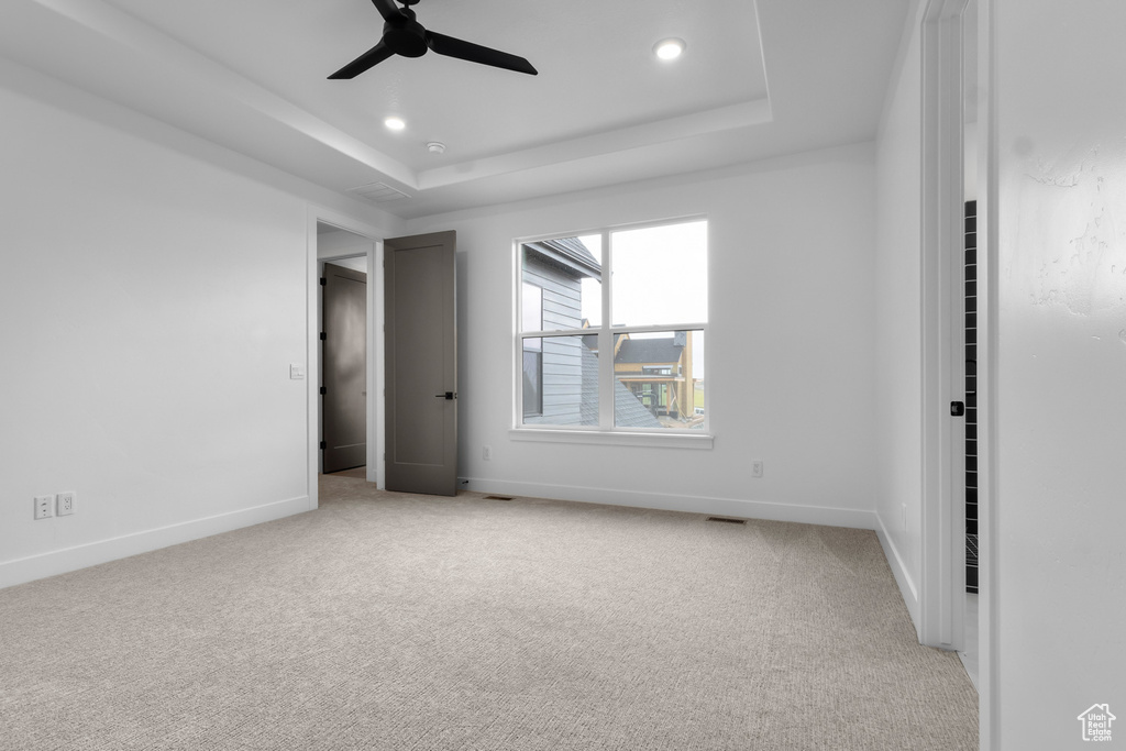 Unfurnished bedroom featuring light carpet, a tray ceiling, recessed lighting, and a ceiling fan