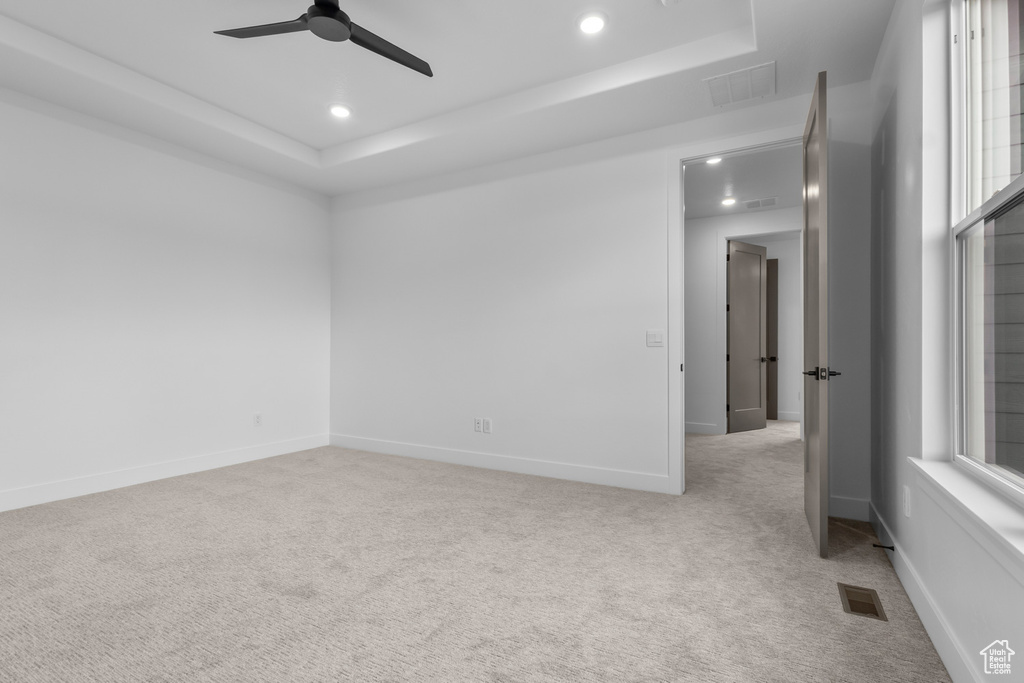 Empty room featuring a raised ceiling, light carpet, recessed lighting, and ceiling fan