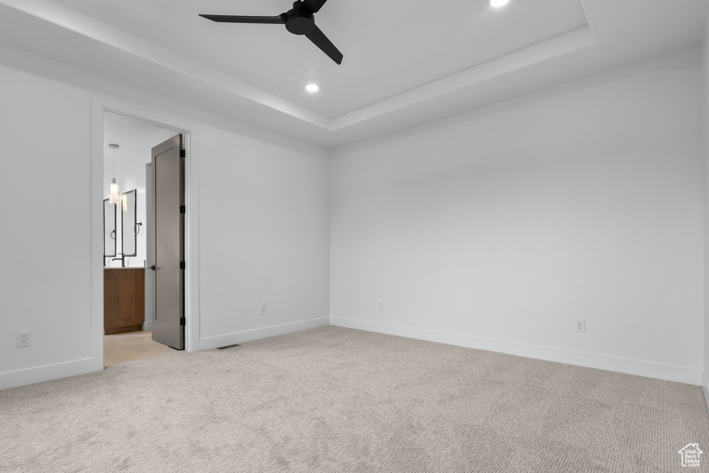 Empty room featuring a raised ceiling, light colored carpet, a ceiling fan, and recessed lighting
