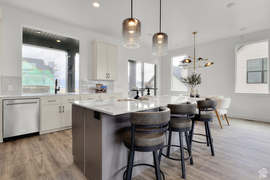 Kitchen with dishwasher, light wood-style flooring, backsplash, a kitchen island, and a breakfast bar area