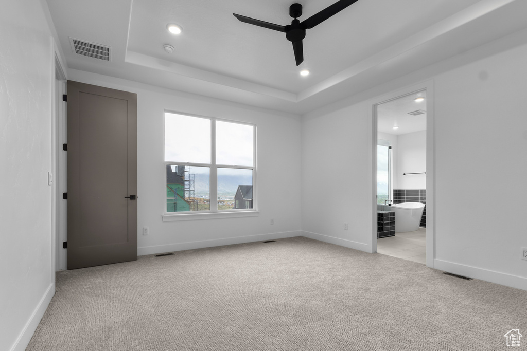 Unfurnished bedroom with light colored carpet, a tray ceiling, ensuite bath, and recessed lighting