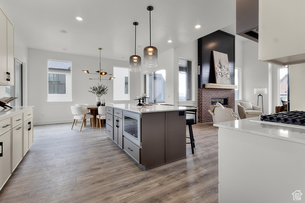 Kitchen featuring a brick fireplace, gas cooktop, light wood-style floors, stainless steel microwave, and a breakfast bar