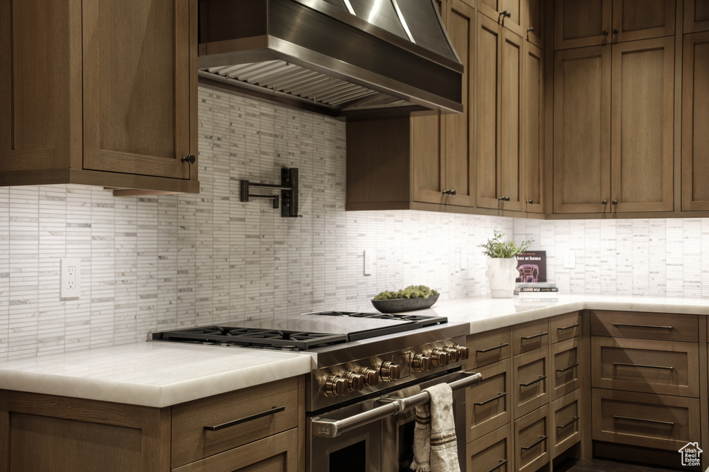Kitchen with high end range, wall chimney range hood, tasteful backsplash, and light countertops
