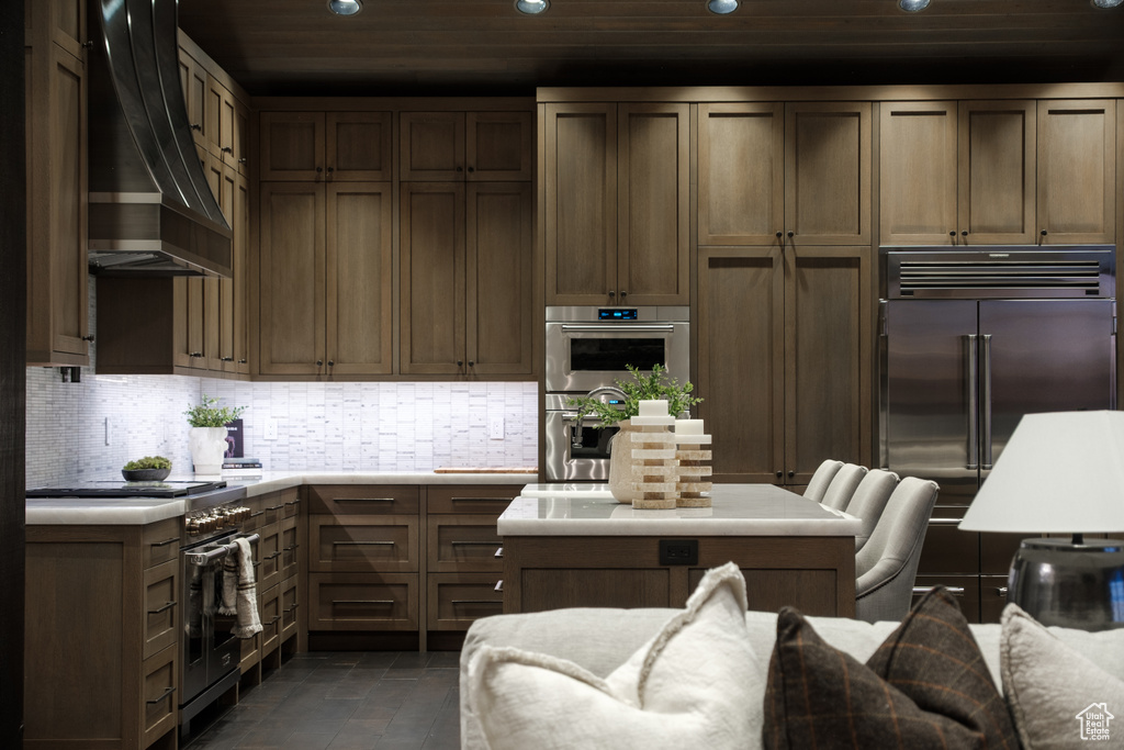Kitchen with high quality appliances, wall chimney range hood, recessed lighting, light countertops, and backsplash