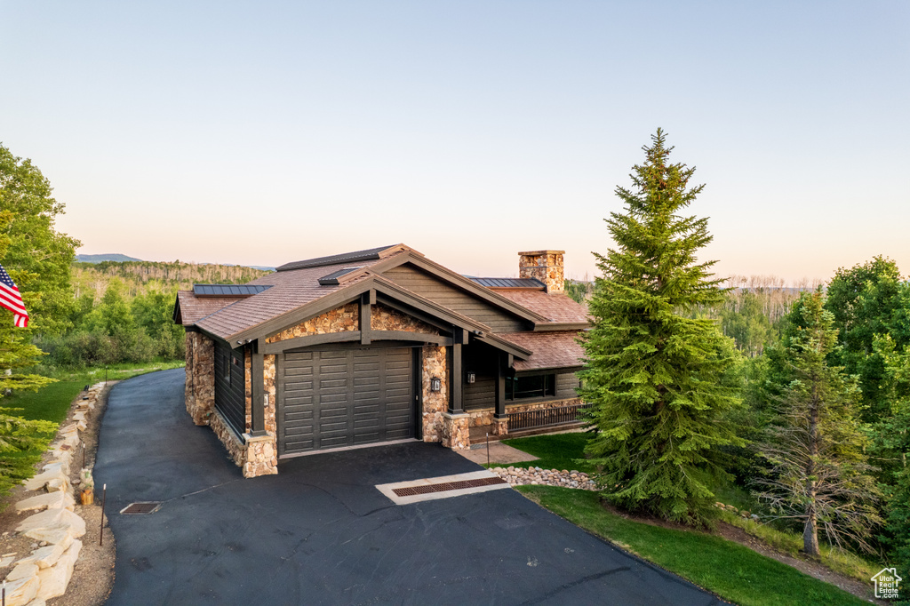 View of front facade with stone siding, asphalt driveway, a chimney, roof mounted solar panels, and an attached garage