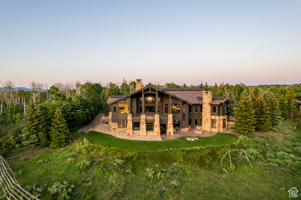 Back of property at dusk with stone siding, a chimney, a patio, and a lawn