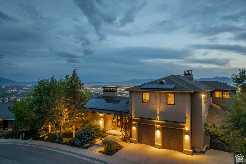 View of front facade with an attached garage, a chimney, roof mounted solar panels, and a mountain view