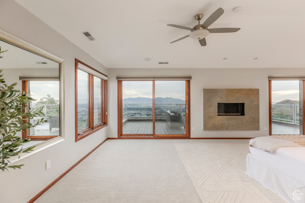 Bedroom with access to exterior, multiple windows, a high end fireplace, and ceiling fan