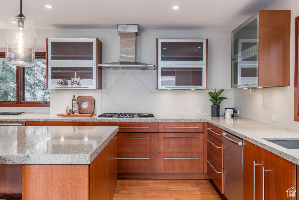 Kitchen featuring wall chimney range hood, stainless steel appliances, brown cabinetry, modern cabinets, and recessed lighting