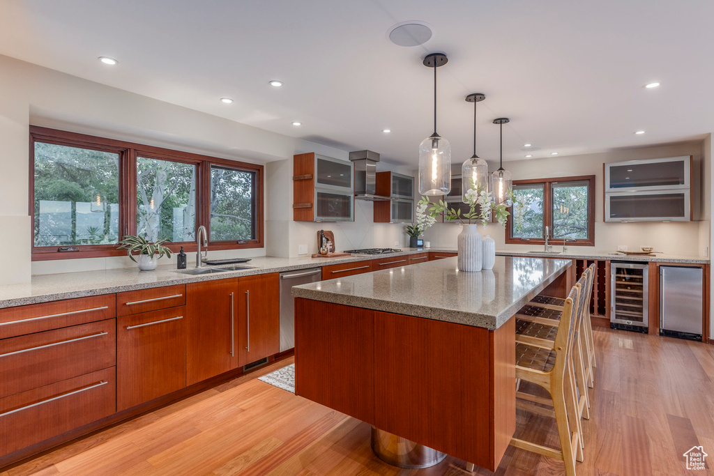 Kitchen with wine cooler, appliances with stainless steel finishes, recessed lighting, light wood-type flooring, and light stone countertops