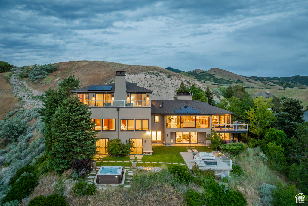 Back of house featuring a balcony, roof mounted solar panels, a patio area, a mountain view, and stucco siding