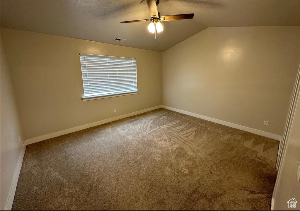 Carpeted empty room featuring a ceiling fan and vaulted ceiling
