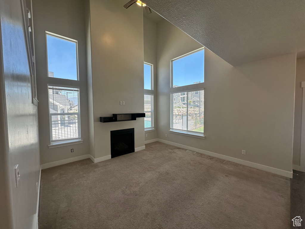 Unfurnished living room featuring carpet, a fireplace, healthy amount of natural light, a textured ceiling, and a high ceiling