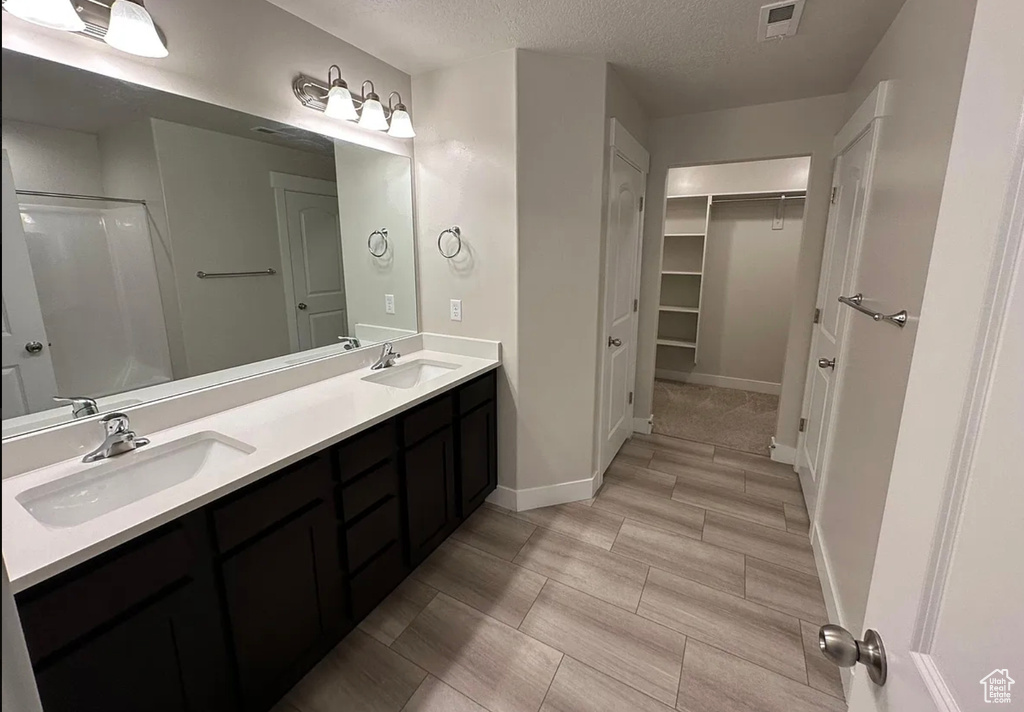 Full bathroom featuring a walk in closet, double vanity, a textured ceiling, and a shower