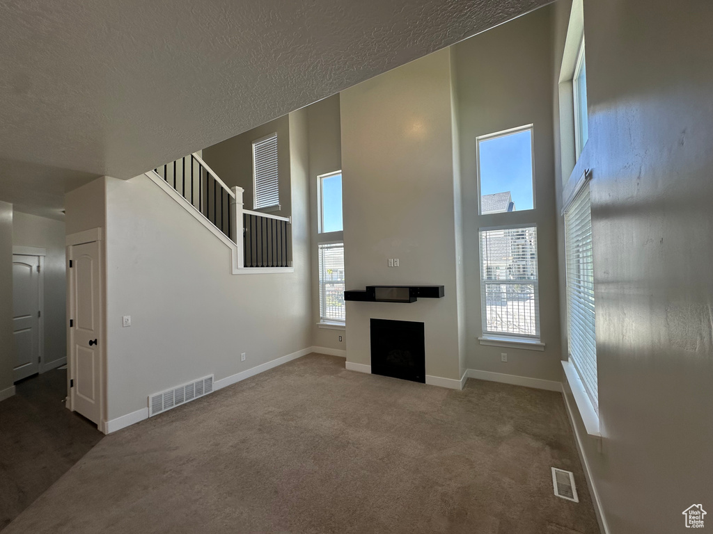 Unfurnished living room featuring a towering ceiling, carpet, a fireplace, a textured ceiling, and stairs