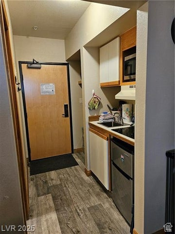 Kitchen with white cabinets, dark wood-type flooring, stainless steel microwave, under cabinet range hood, and light countertops