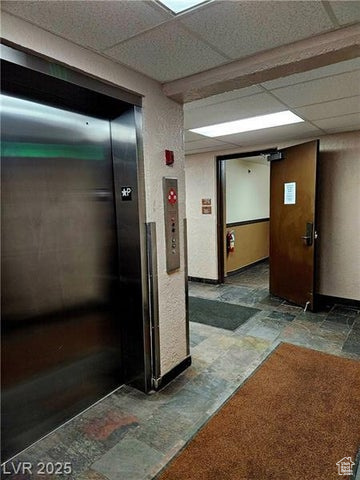 Corridor featuring stone tile floors, elevator, and a drop ceiling