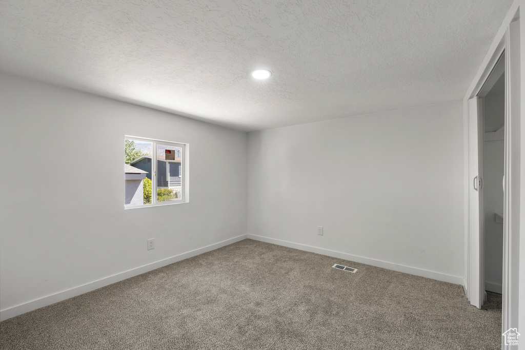 Carpeted empty room with a textured ceiling and recessed lighting