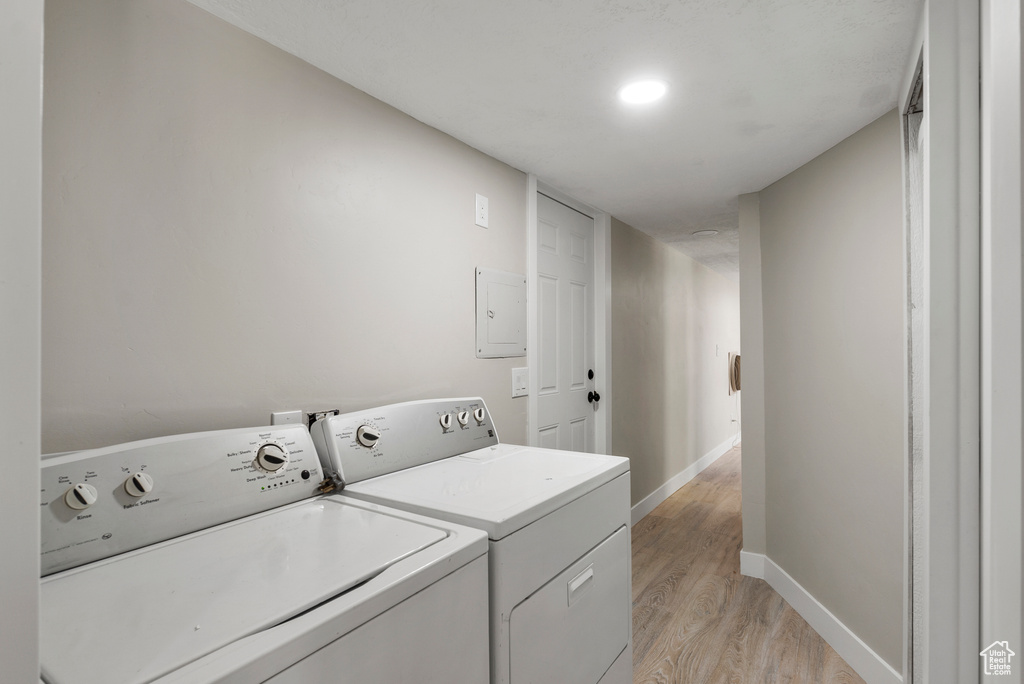 Laundry area with light wood-style floors, washing machine and clothes dryer, and electric panel