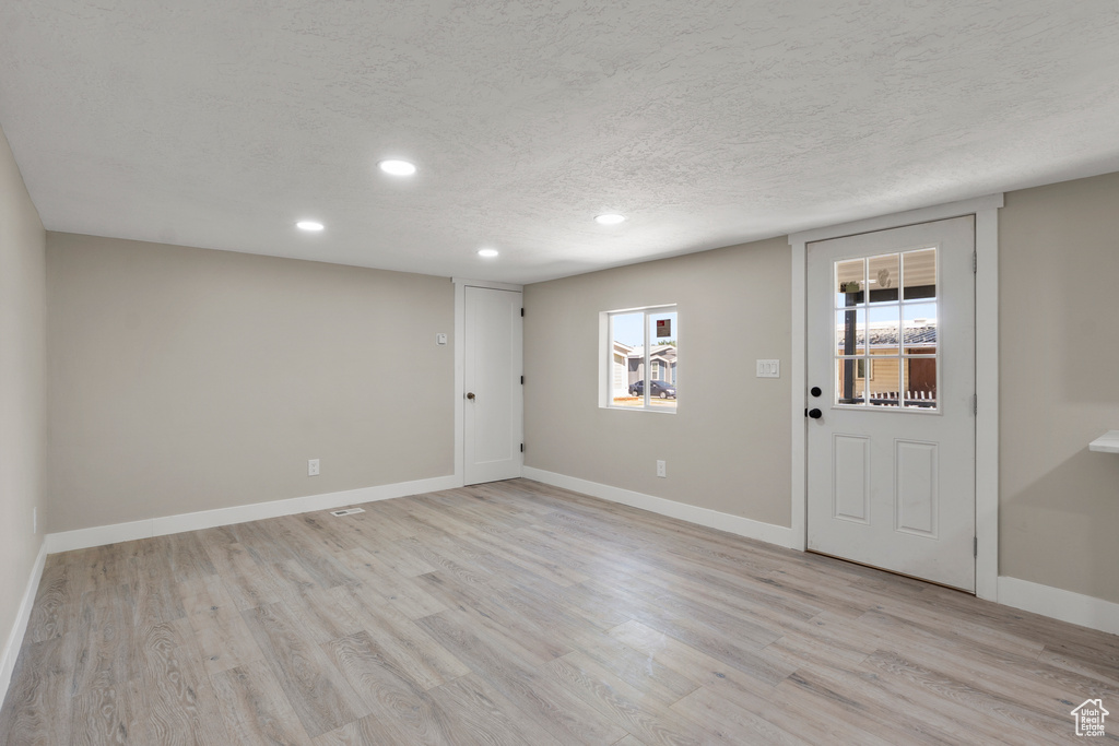 Below grade area featuring recessed lighting, light wood-type flooring, and a textured ceiling