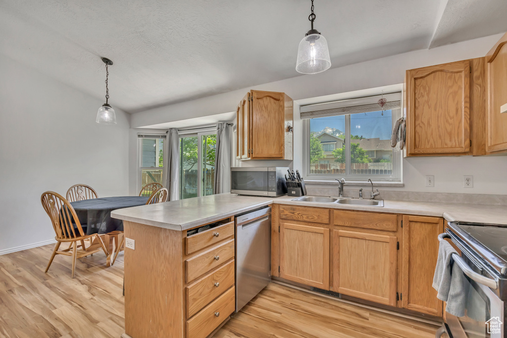 Kitchen featuring appliances with stainless steel finishes, a peninsula, plenty of natural light, light countertops, and vaulted ceiling