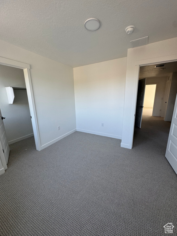 Unfurnished bedroom featuring dark colored carpet and a textured ceiling