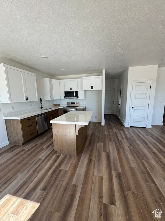 Kitchen with stainless steel appliances, white cabinetry, a center island, dark wood-style floors, and a textured ceiling