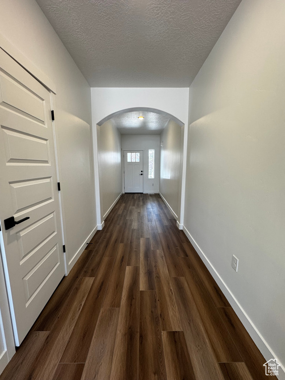 Hallway featuring arched walkways, a textured ceiling, and dark wood finished floors