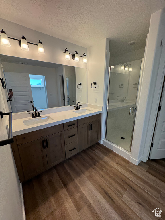 Full bathroom with wood finished floors, a textured ceiling, double vanity, and a stall shower