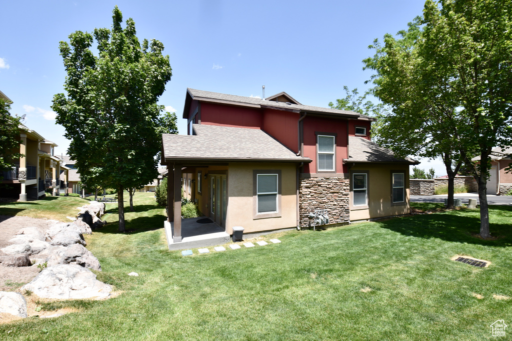 Back of property featuring stucco siding, a yard, stone siding, and a shingled roof