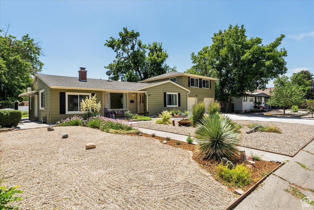 View of front of house with an attached garage, a chimney, and driveway